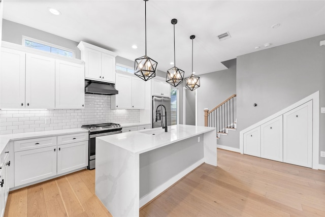 1412 Weiss St, Houston, TX 77009 - kitchen featuring stainless steel appliances, under cabinet range hood, light wood-style floors, backsplash, and an island with sink