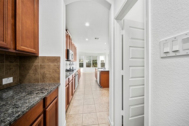 4663 Rockton Hills Ln, Sugar Land, TX 77479 - kitchen featuring stainless steel microwave, dark stone counters, brown cabinetry, light tile patterned flooring, and recessed lighting
