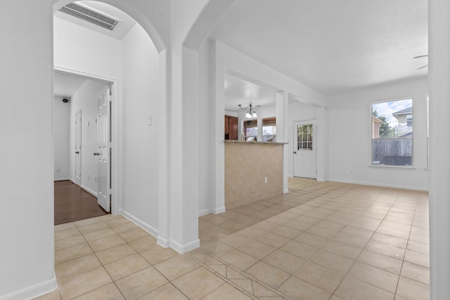 unfurnished living room featuring light tile patterned floors, arched walkways, and baseboards
