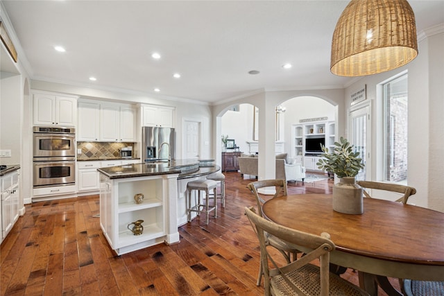 6338 Collina Springs Ct, Houston, TX 77041 - kitchen featuring arched walkways, ornamental molding, appliances with stainless steel finishes, open shelves, and a center island with sink