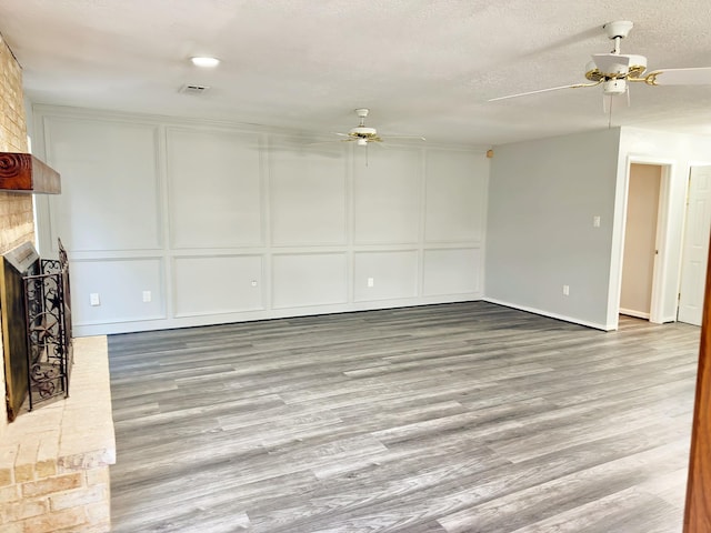 16007 Sailfin St, Crosby, TX 77532 - unfurnished living room featuring a decorative wall, a ceiling fan, a brick fireplace, wood finished floors, and a textured ceiling