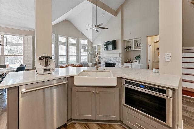 31 Brywood Pl, The Woodlands, TX 77382 - kitchen featuring appliances with stainless steel finishes, a sink, open floor plan, a fireplace, and light wood-type flooring