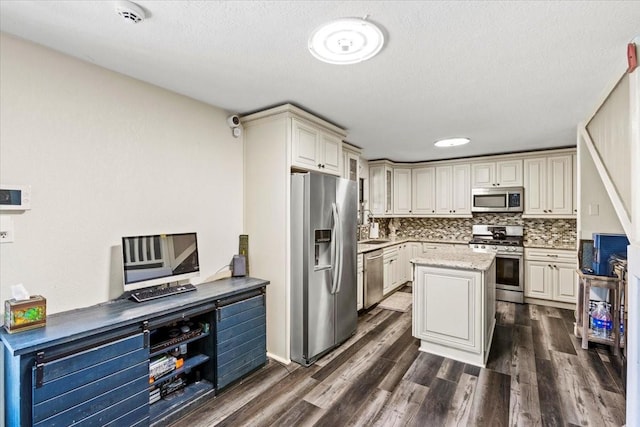 kitchen with appliances with stainless steel finishes, dark wood finished floors, a center island, backsplash, and cream cabinets