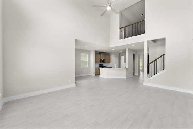 18423 Windy Knoll Way, Houston, TX 77084 - unfurnished living room with ceiling fan, baseboards, stairway, light wood-type flooring, and a towering ceiling