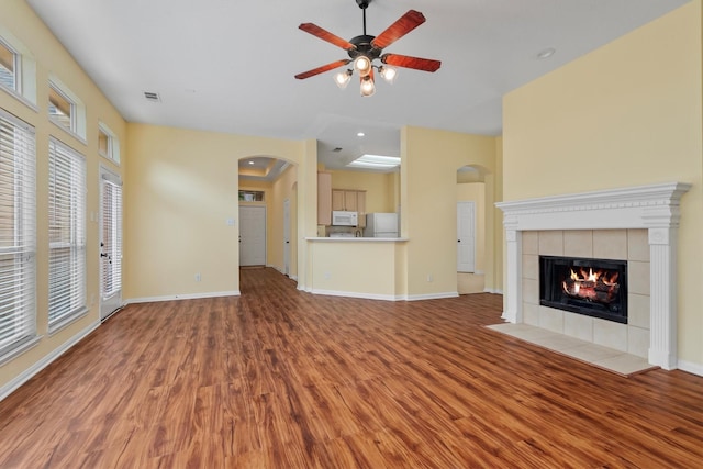 13014 Vivienne Westmoreland Dr, Cypress, TX 77429 - unfurnished living room with arched walkways, light wood-style floors, a ceiling fan, a tile fireplace, and baseboards