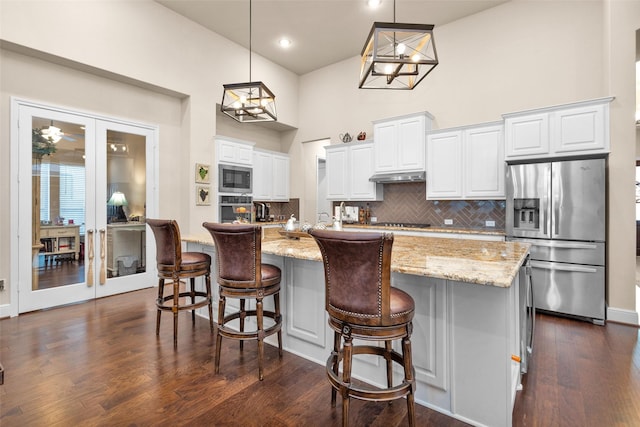 15527 Salmon Springs Dr, Conroe, TX 77302 - kitchen with appliances with stainless steel finishes, decorative backsplash, a towering ceiling, under cabinet range hood, and light stone countertops
