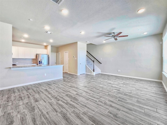 unfurnished living room featuring a ceiling fan, stairway, light wood finished floors, baseboards, and recessed lighting