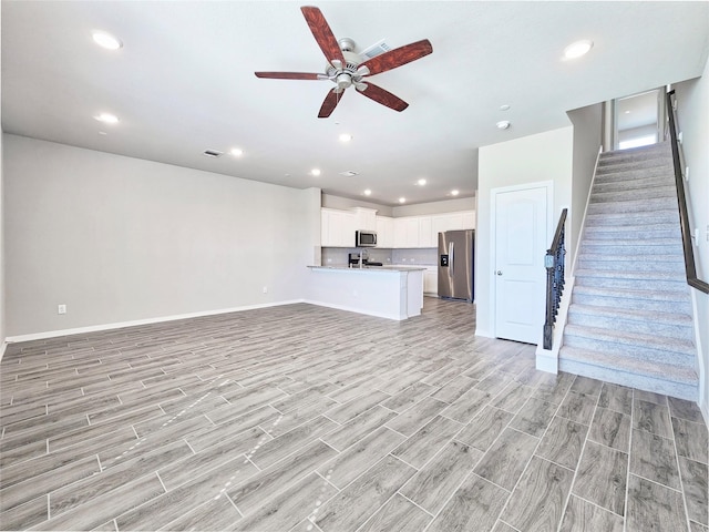unfurnished living room with stairway, light wood finished floors, a ceiling fan, baseboards, and recessed lighting