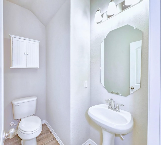 bathroom with wood finished floors, toilet, a sink, baseboards, and lofted ceiling