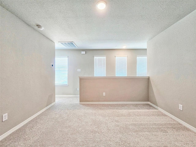 carpeted empty room featuring a textured ceiling, a textured wall, and baseboards