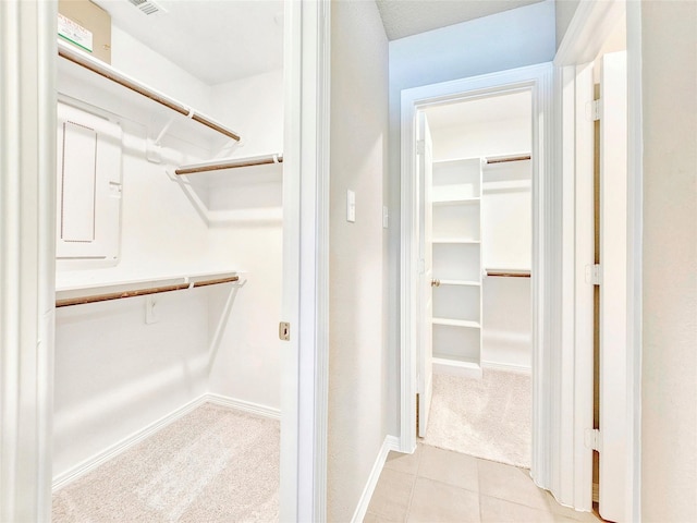 walk in closet featuring electric panel, light tile patterned floors, and light carpet