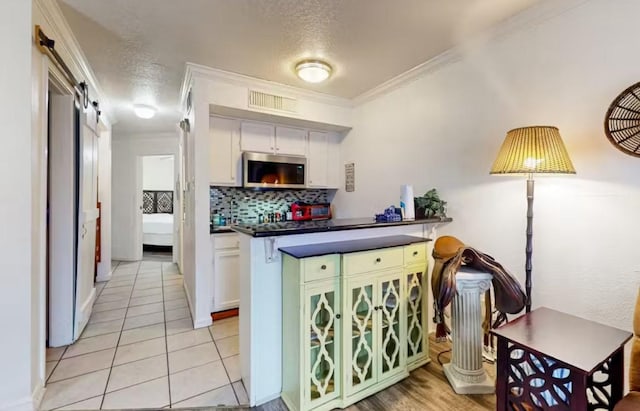6300 Seawall Blvd Unit 3113, Galveston, TX 77551 - kitchen featuring stainless steel microwave, tasteful backsplash, dark countertops, white cabinets, and ornamental molding