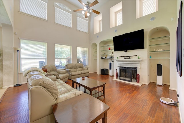 2127 Linden Rock Dr, Katy, TX 77494 - living area with a ceiling fan, built in features, a glass covered fireplace, wood finished floors, and a high ceiling
