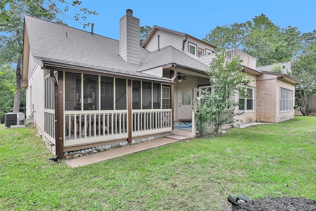 rear view of property featuring central AC, a chimney, a shingled roof, a sunroom, and a lawn