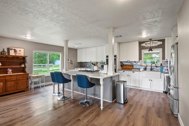 kitchen with white cabinetry, wood finished floors, decorative backsplash, a breakfast bar area, and healthy amount of natural light