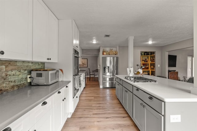 kitchen featuring stainless steel appliances, light wood-style floors, light countertops, backsplash, and white cabinetry