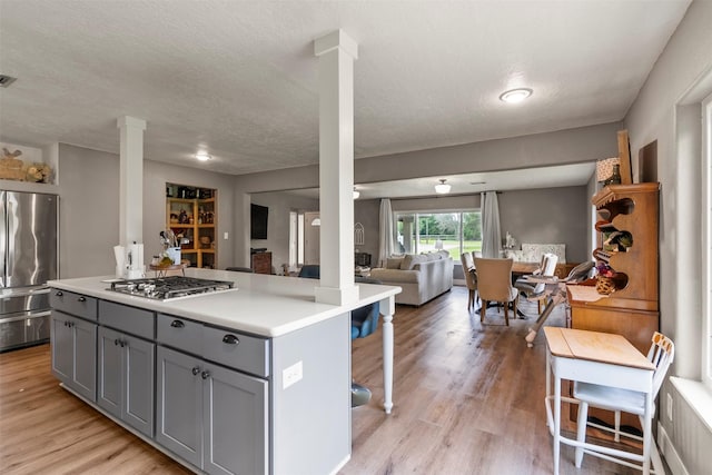kitchen featuring stainless steel appliances, ornate columns, gray cabinets, open floor plan, and light countertops