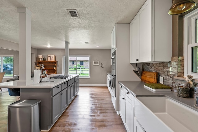 kitchen with decorative columns, gray cabinets, white cabinetry, wood finished floors, and backsplash
