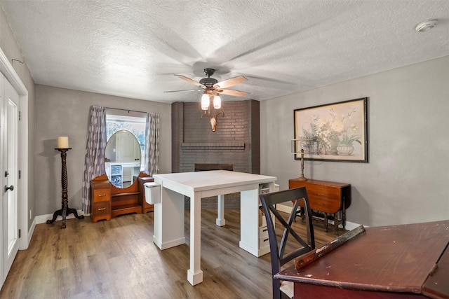 office area featuring a ceiling fan, wood finished floors, a brick fireplace, a textured ceiling, and baseboards