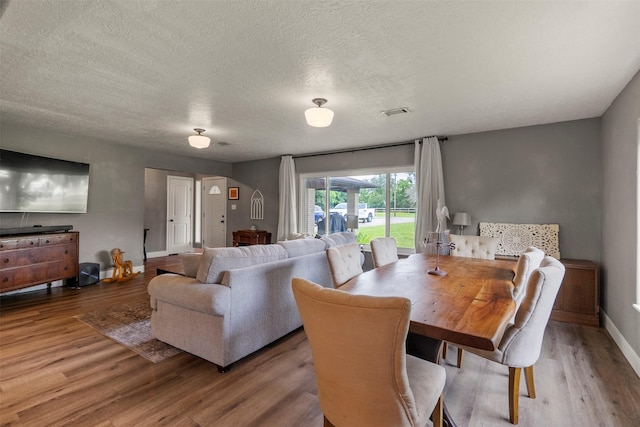 dining room with wood finished floors, a textured ceiling, and baseboards