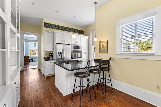 1427 Winnie St, Galveston, TX 77550 - kitchen featuring appliances with stainless steel finishes, dark wood-type flooring, a breakfast bar, white cabinetry, and dark countertops