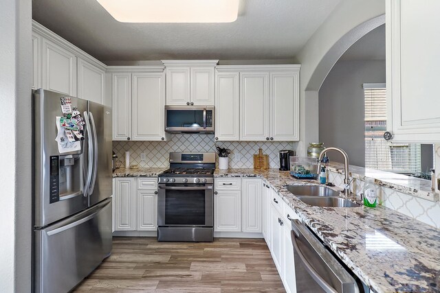 4418 Legends Bay Dr, Baytown, TX 77523 - kitchen featuring appliances with stainless steel finishes, a sink, arched walkways, white cabinetry, and light wood-type flooring