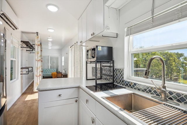 1350 23rd St, San Leon, TX 77539 - kitchen with a sink, a wall unit AC, light wood-style floors, white cabinetry, and decorative backsplash