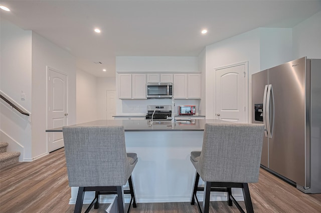 40434 Basalt Elm Rd, Magnolia, TX 77354 - kitchen with appliances with stainless steel finishes, wood finished floors, white cabinets, a breakfast bar area, and recessed lighting