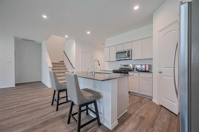 40434 Basalt Elm Rd, Magnolia, TX 77354 - kitchen featuring appliances with stainless steel finishes, a sink, wood finished floors, a breakfast bar, and white cabinets