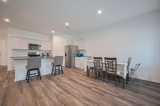 40434 Basalt Elm Rd, Magnolia, TX 77354 - kitchen with stainless steel appliances, dark wood-type flooring, a kitchen island with sink, white cabinets, and a kitchen bar