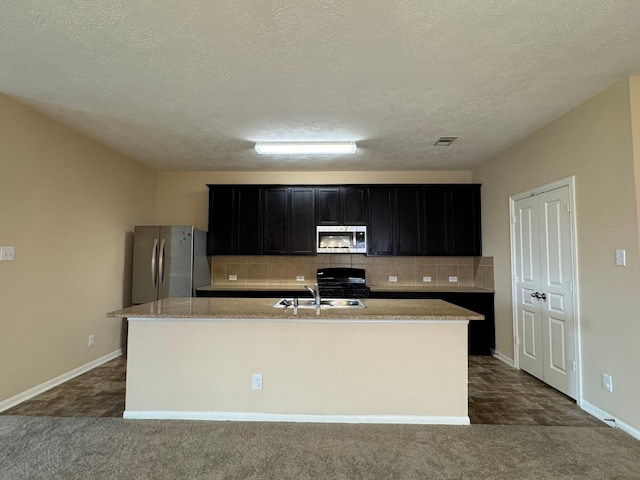 42 Blisten Spring Dr, Manvel, TX 77578 - kitchen with stainless steel appliances, dark cabinets, a sink, a kitchen island with sink, and decorative backsplash