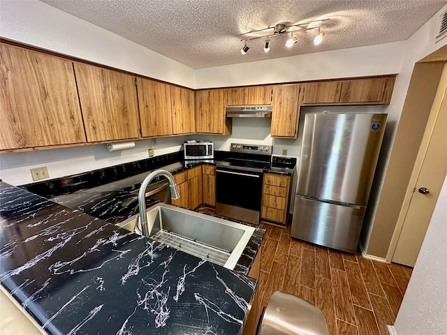 2611 Grants Lake Blvd Unit 237, Sugar Land, TX 77479 - kitchen featuring stainless steel appliances, under cabinet range hood, brown cabinetry, a textured ceiling, and a sink
