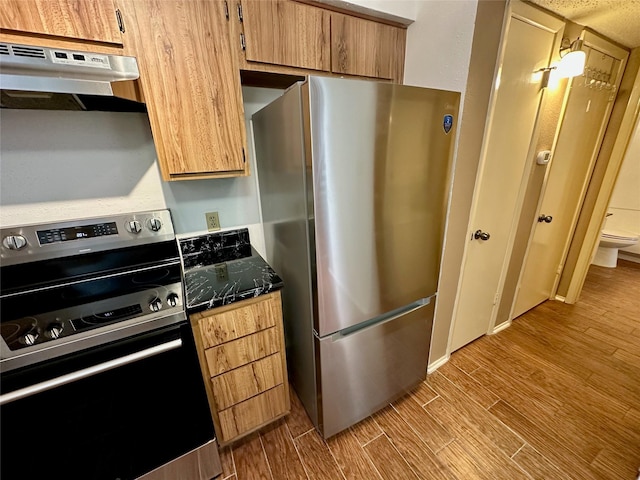 2611 Grants Lake Blvd Unit 237, Sugar Land, TX 77479 - kitchen with appliances with stainless steel finishes, under cabinet range hood, wood finished floors, dark countertops, and brown cabinets