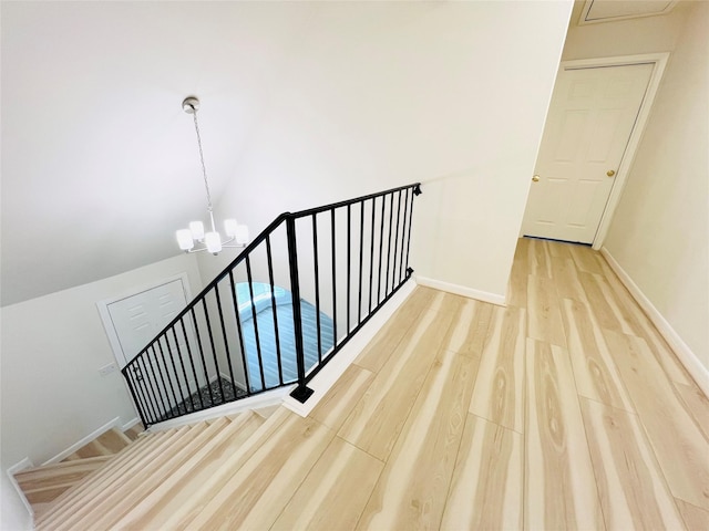 stairway with wood finished floors, a chandelier, vaulted ceiling, and baseboards