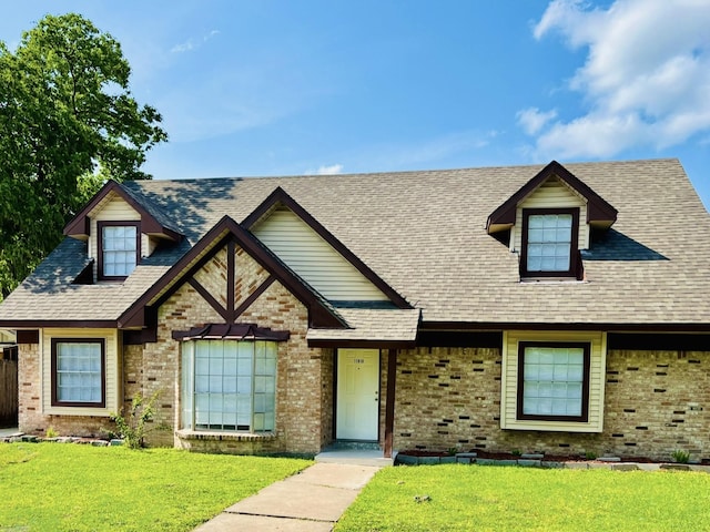 tudor-style house with brick siding, a front yard, and roof with shingles