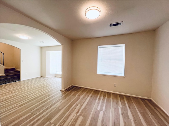 unfurnished room featuring arched walkways, light wood finished floors, stairway, and baseboards