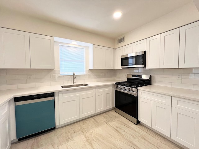 kitchen with stainless steel appliances, a sink, tasteful backsplash, and white cabinetry
