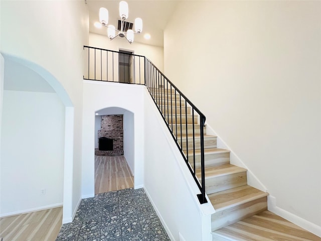 stairway with a chandelier, arched walkways, baseboards, a brick fireplace, and a towering ceiling