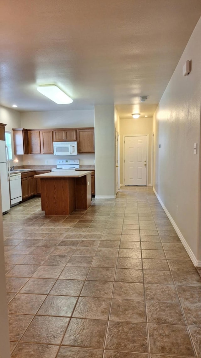 kitchen with white appliances, light countertops, a kitchen island, baseboards, and brown cabinets