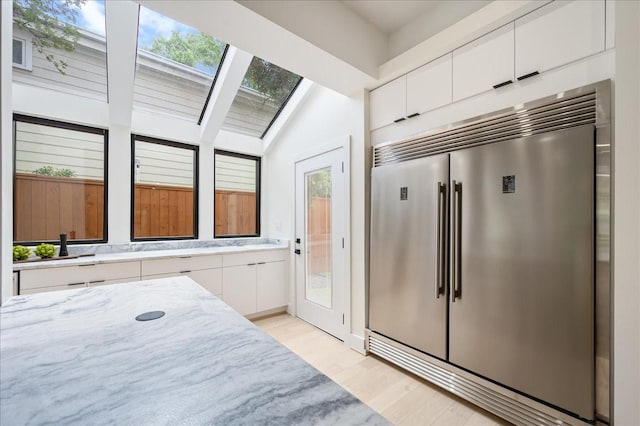 2135 Quenby St, Houston, TX 77005 - kitchen with stainless steel built in fridge, white cabinetry, light wood-style flooring, and light stone countertops