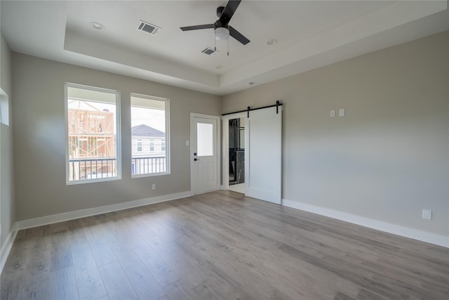 6535 Cohn St, Houston, TX 77091 - unfurnished bedroom featuring a tray ceiling, a barn door, wood finished floors, baseboards, and a ceiling fan