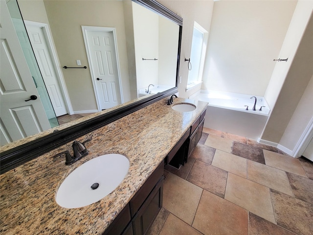 bathroom with a bath, stone tile flooring, double vanity, and baseboards