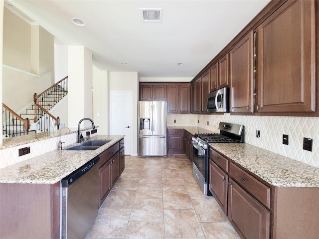 kitchen with appliances with stainless steel finishes, a sink, tasteful backsplash, and light stone counters