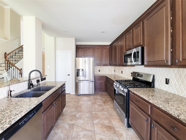 kitchen with stainless steel appliances, a sink, light stone countertops, and tasteful backsplash