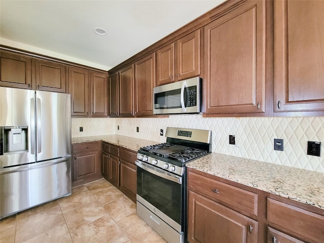 kitchen featuring appliances with stainless steel finishes, backsplash, light stone counters, and light tile patterned flooring