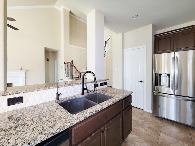 kitchen with appliances with stainless steel finishes, a sink, light stone counters, dark brown cabinets, and ceiling fan