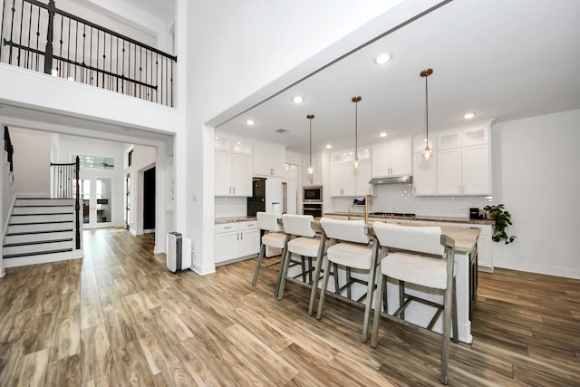 17355 Camillia Trl, Conroe, TX 77302 - kitchen featuring under cabinet range hood, tasteful backsplash, a breakfast bar area, wood finished floors, and recessed lighting