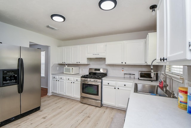 16023 Mission Glen Dr, Houston, TX 77083 - kitchen featuring appliances with stainless steel finishes, under cabinet range hood, light countertops, a sink, and white cabinets