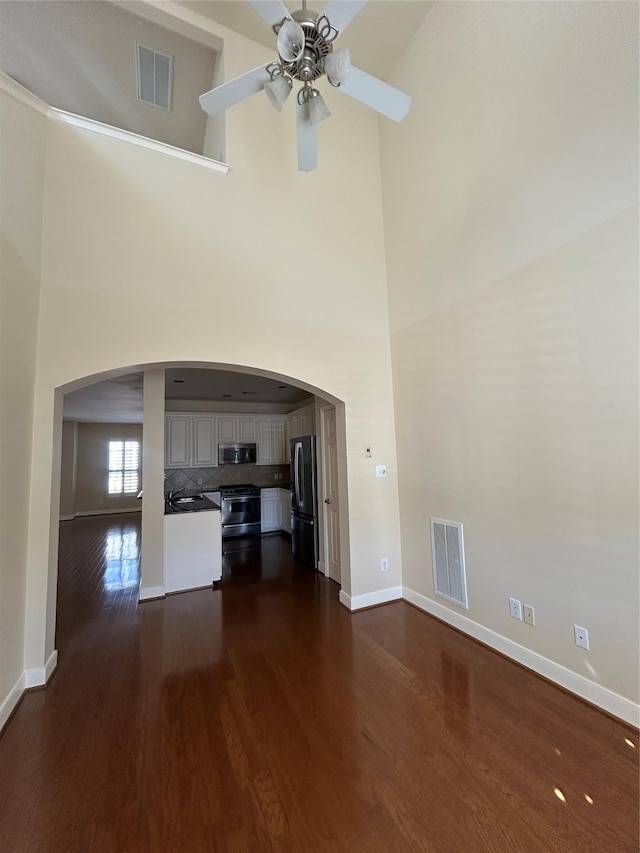 2333 Ann St, Houston, TX 77003 - unfurnished living room featuring a towering ceiling, dark wood-type flooring, baseboards, arched walkways, and a ceiling fan