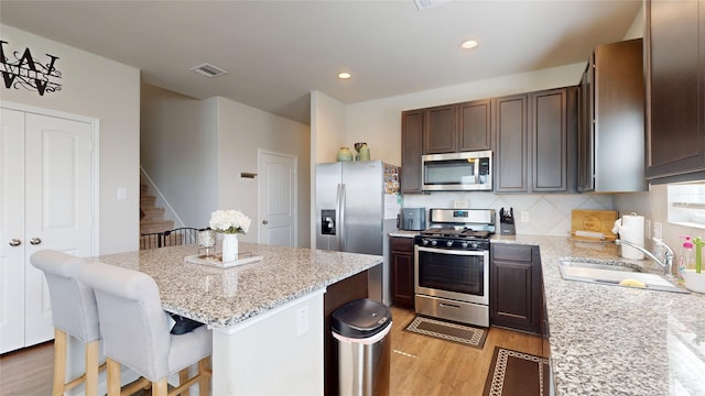 24803 Signorelli Way, Katy, TX 77493 - kitchen with stainless steel appliances, a sink, light wood finished floors, a kitchen island, and light stone countertops